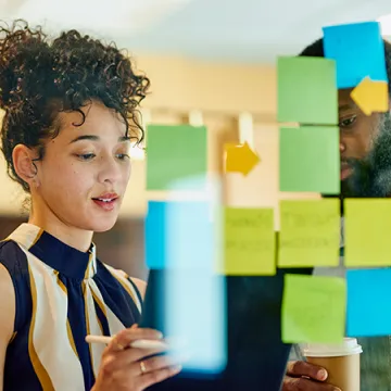 A woman looks a post-it notes on a glass wall.