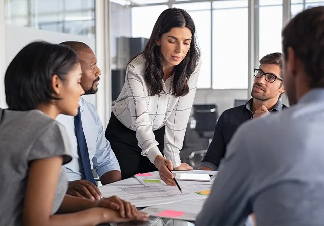 People sitting around a table discussing documents with one person pointing out a specific detail on a document.