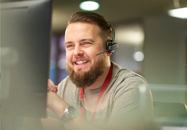 A man sitting in front of a computer screen wearing a headset.