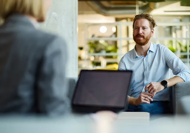 A person sitting in front of a laptop talking to another person opposite them.