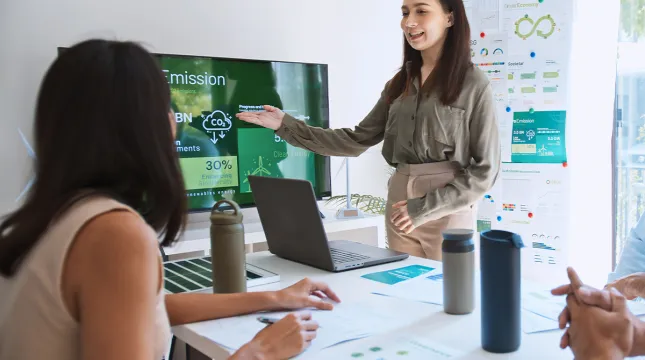 A woman pointing at a screen that displays information on carbon emissions.