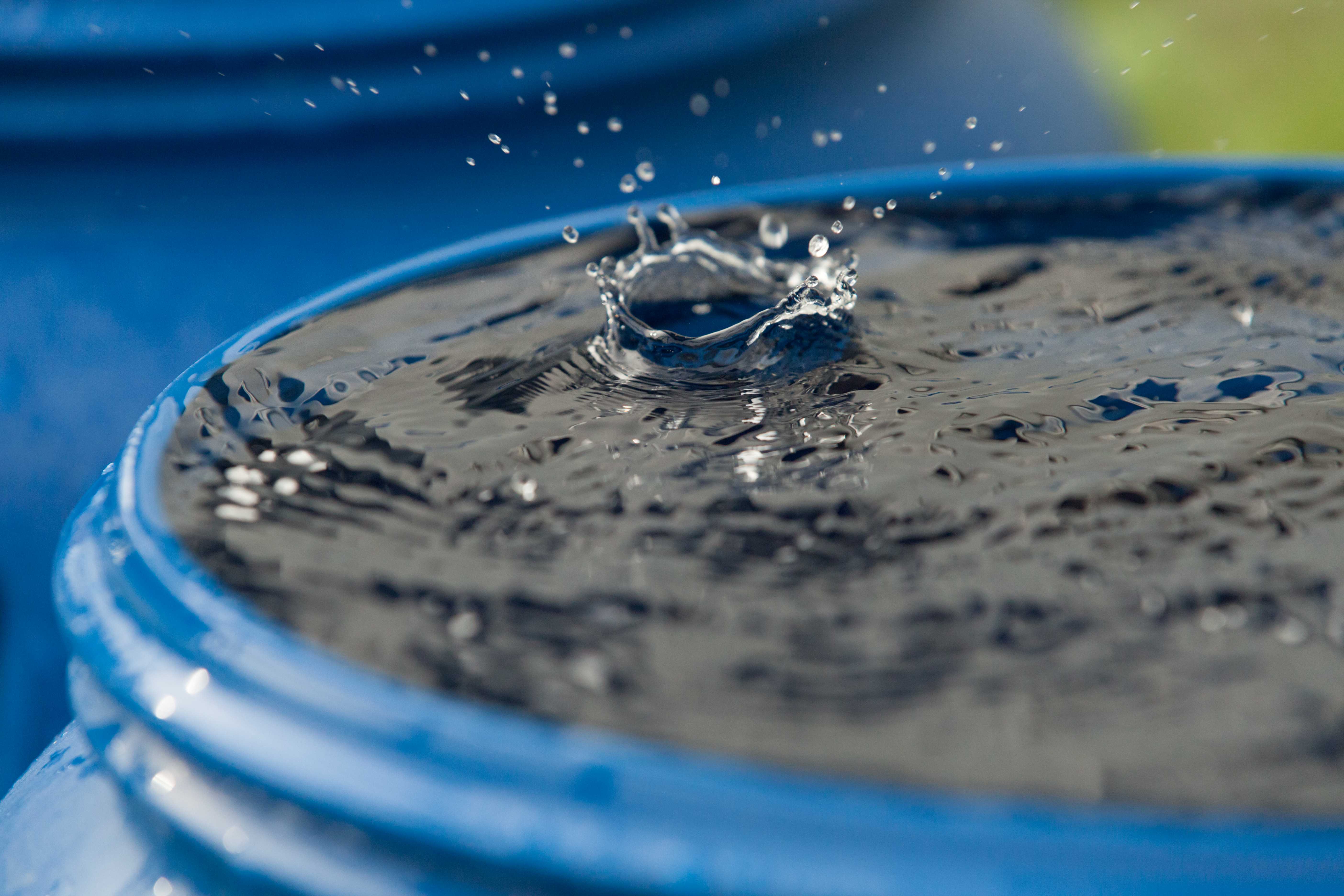 A barrel filled with water with one droplet splashing into it.